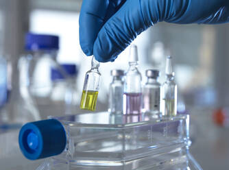 Hand of person wearing protective glove picking up pharmaceutical vial in laboratory - ABRF00719