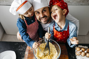 Portrait of happy father with two kids preparing dough in kitchen at home - JRFF04273
