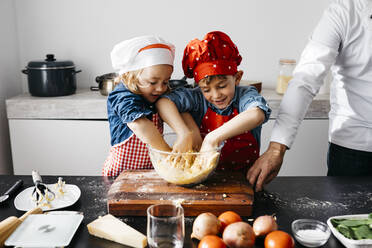 Kinder bereiten mit ihrem Vater in der Küche zu Hause Teig vor - JRFF04278