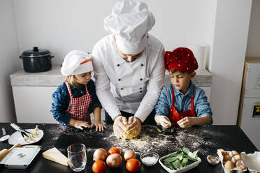 Vater mit zwei Kindern bei der Zubereitung selbstgemachter glutenfreier Nudeln in der Küche zu Hause - JRFF04286