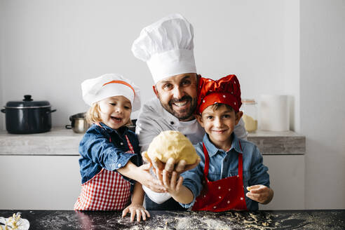 Porträt eines Vaters mit zwei Kindern bei der Zubereitung von Teig in der Küche zu Hause - JRFF04287