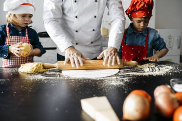 Vater mit zwei Kindern bei der Zubereitung von Teig für selbstgemachte glutenfreie Nudeln in der Küche zu Hause - JRFF04288