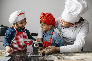 Vater mit zwei Kindern macht hausgemachte Nudeln mit Nudelmaschine in der Küche zu Hause - JRFF04293