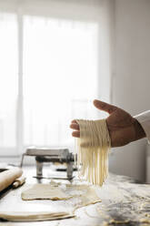 Hand holding homemade gluten free pasta in kitchen at home - JRFF04298