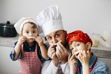 Playful father with two kids having fun while preparing homemade pasta in kitchen at home - JRFF04299