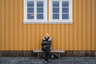 Tourist sitzt auf einer Bank bei einer Hütte, Lofoten, Norwegen - MPPF00705