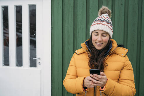 Smiling tourist using cell phone at a hut, Lofoten, Norway - MPPF00707