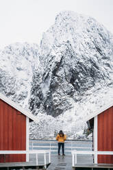 Tourist steht an einer Hütte an der Küste, Lofoten, Norwegen - MPPF00710