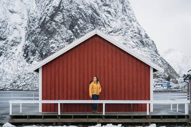 Tourist steht an einer Hütte an der Küste, Lofoten, Norwegen - MPPF00711