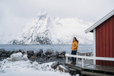 Tourist steht an einer Hütte an der Küste, Lofoten, Norwegen - MPPF00712