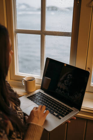 Frau mit Laptop am Fenster, lizenzfreies Stockfoto