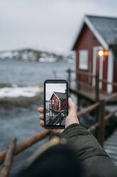 Nahaufnahme eines Touristen, der ein Handyfoto an der Küste macht, Lofoten, Norwegen - MPPF00735