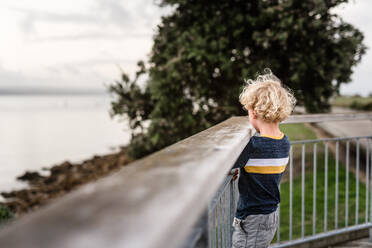 Curly haired child looking over railing in Napier, New Zealand - CAVF78184