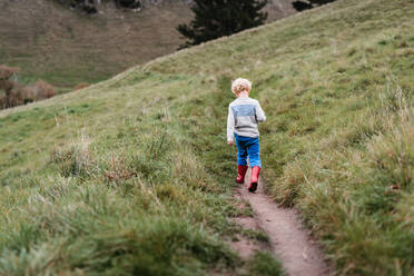 Kleiner Junge mit lockigen Haaren geht auf einem Pfad am Hang spazieren - CAVF78197