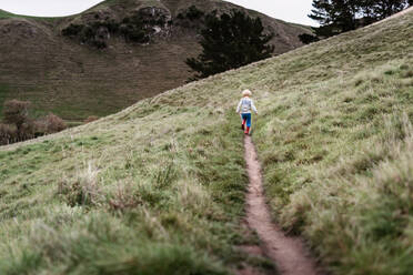 Young child hiking on path through grassy hillside - CAVF78198