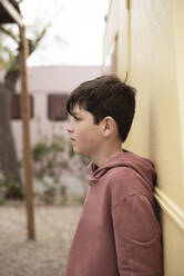 Portrait of a teenage boy leaning against wall looking away - CAVF78356