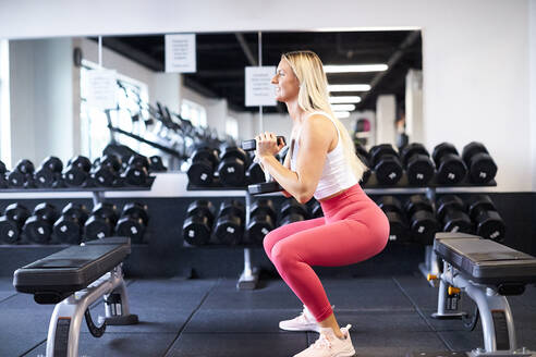 Eine Frau hockt mit einer Hantel im Fitnessstudio. - CAVF78378