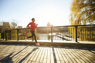 A backlit woman running over a footbridge in a city park. - CAVF78394