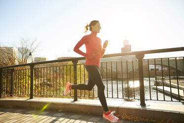 A woman running across a bridge in an urban park. - CAVF78395