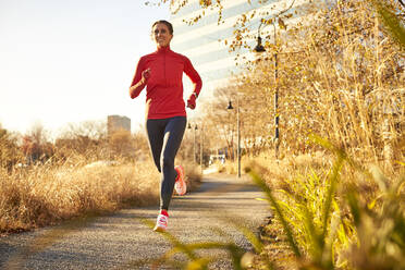 A woman running in an urban park on a bright autumnal day. - CAVF78402