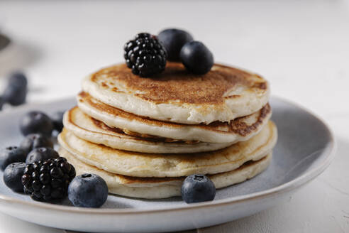 Stack of pancakes with berries on top on a white surface - CAVF78558