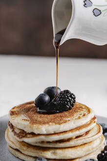 A jar pouring syrup on top of a stack of homemade pancakes with - CAVF78559