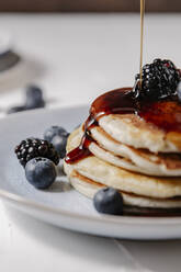 Close up of syrup pouring down a stack of pancakes with berries on top - CAVF78560