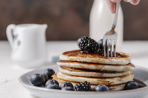 Woman sticking a fork into a stack of homemade pancakes - CAVF78561