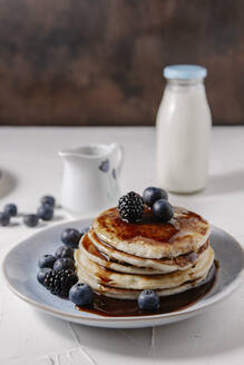 Pancakes topped with syrup and berries, with a bottle of milk in the background - CAVF78563