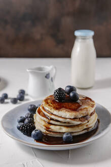 Pfannkuchen mit Sirup und Beeren, mit einer Flasche Milch im Hintergrund - CAVF78563