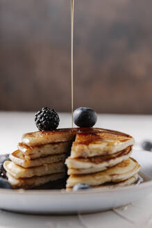 Someone is pouring syrup on top of a stack of homemade pancakes - CAVF78569