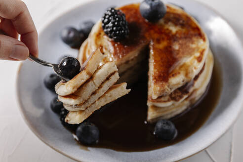 Woman sticking pancakes with a blueberry on a fork - CAVF78573