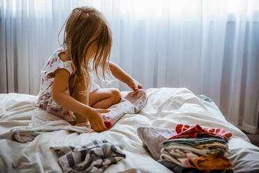 4 Jahre altes Mädchen faltet Handtücher auf einem Bett - CAVF78688