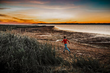 7 Jahre alter Junge, der bei Sonnenaufgang rennt, um Muscheln zu finden - CAVF78689