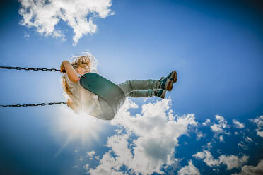 Girl on a swing reaching the clouds on a hot summer afternoon - CAVF78696