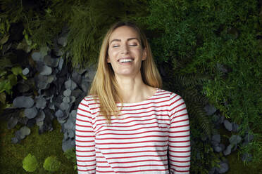Porträt einer glücklichen Frau mit geschlossenen Augen vor einer grünen Wand - RBF07484