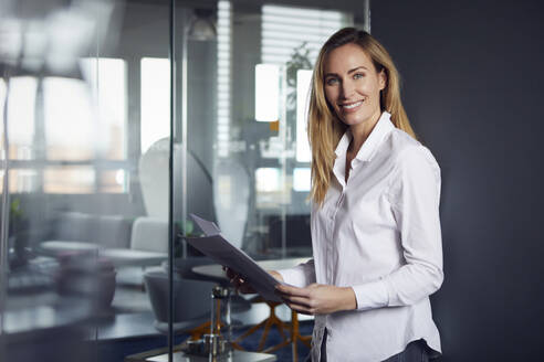 Porträt einer selbstbewussten Geschäftsfrau mit Papieren im Büro - RBF07521
