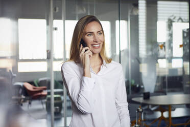 Porträt einer lächelnden Geschäftsfrau am Telefon im Büro - RBF07533