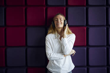 Portrait of happy woman at a purple wall listening to music with headphones - RBF07543