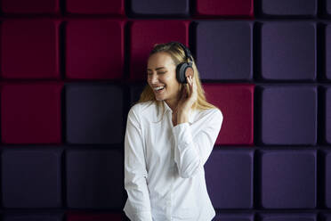 Portrait of happy woman at a purple wall listening to music with headphones - RBF07544