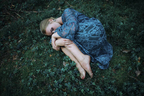 Woman lying on the grass in an embryo pose - CAVF78841