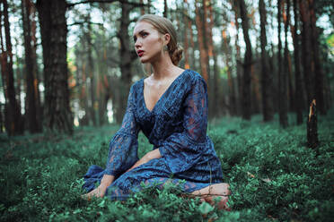 Frau in blauem Kleid sitzend in einem Wald - CAVF78842