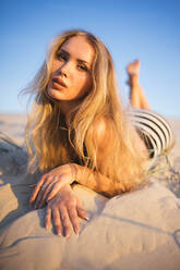 Frau liegt an einem sonnigen Tag auf einem Sandstrand - CAVF78847