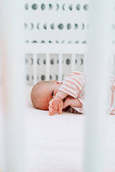 Closeup portrait of a baby girl laying in a modern crib - CAVF78856