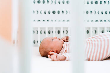 Sideview of a newborn girl laying in her modern crib - CAVF78859