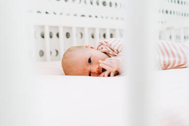 Blick durch ein Kinderbett auf ein neugeborenes Mädchen, das in die Kamera schaut - CAVF78861
