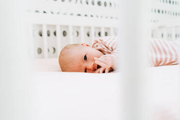 View through a crib of a newborn girl looking at the camera - CAVF78861