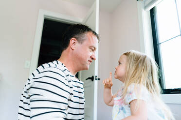 Side view of a toddler motioning for her dad to be quiet - CAVF78870