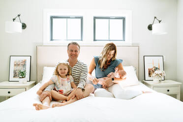Geradliniges Porträt einer vierköpfigen Familie, die zusammen auf einem Bett sitzt - CAVF78886