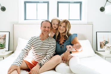 Closeup portrait of a family of four sitting together on a bed - CAVF78889